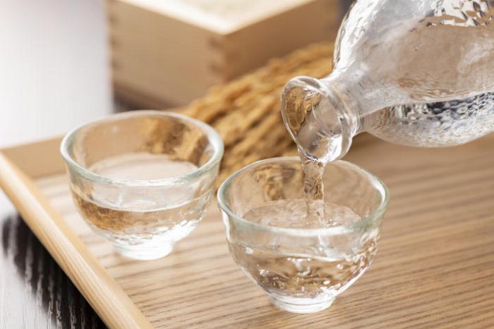 5種類のベース酒（ホワイトリカー、ブランデー、日本酒、焼酎、ウイスキー）のボトルと、それぞれの梅酒が入ったグラスが並んでいる様子